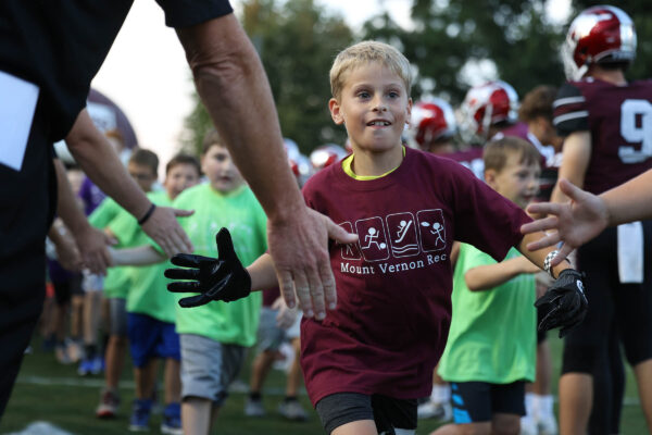Boy running and give high fives to football coaches and players.