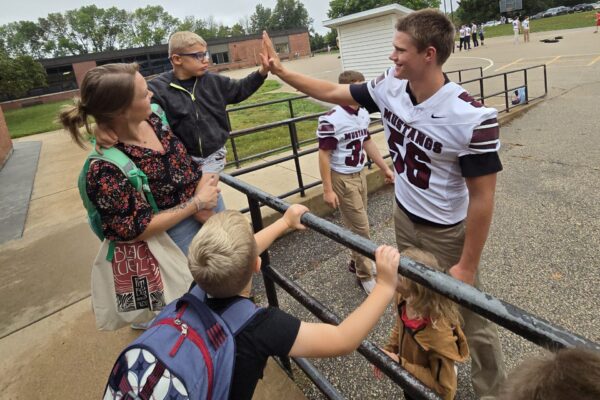 High school football student high-fiving elementary student.